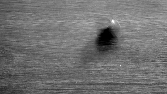 Monochrome film still of coin spinning on a wooden surface